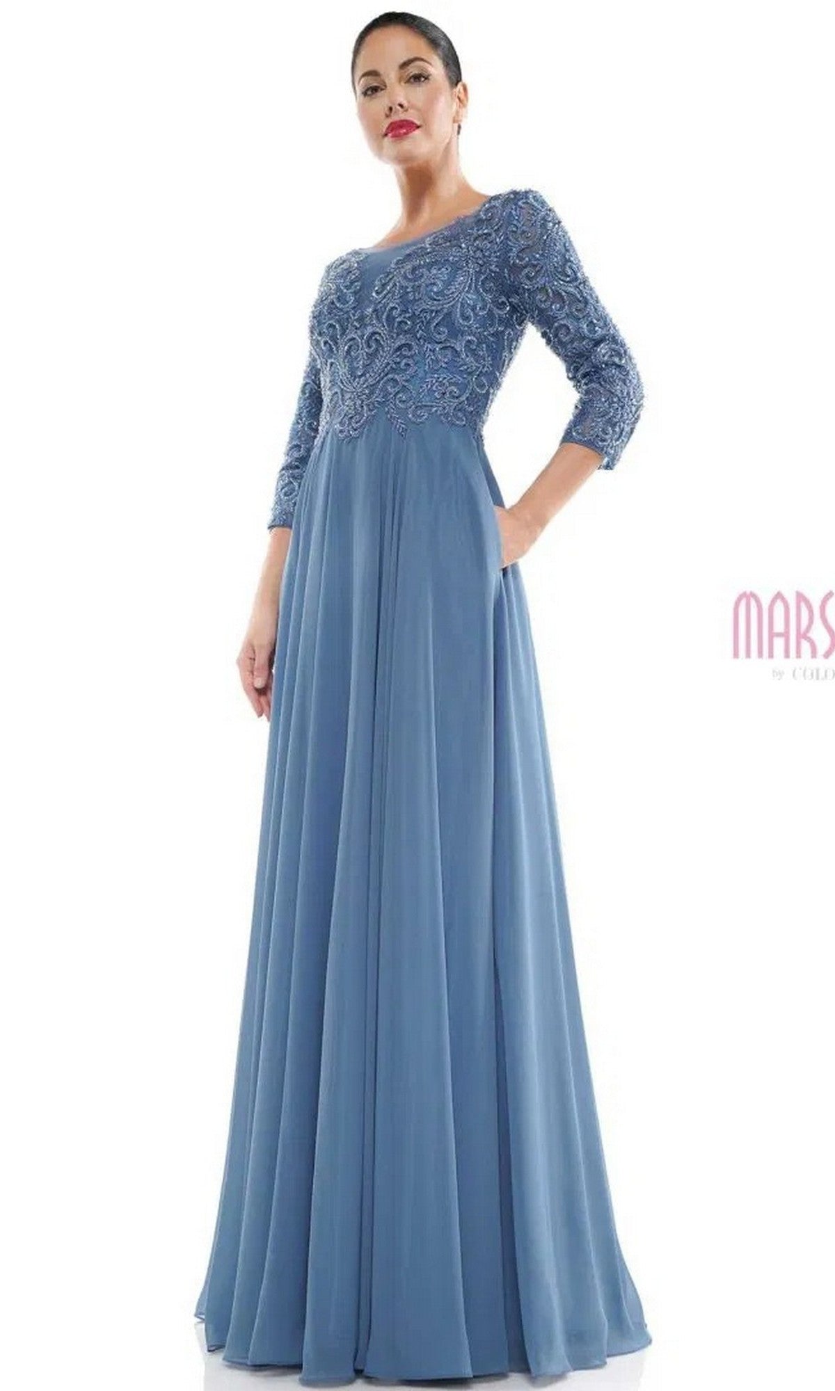 A woman stands against a white background wearing the Marsoni MV1052 long formal dress in slate blue, featuring a beaded bodice, three-quarter lace sleeves, and an elegant chiffon A-line skirt.